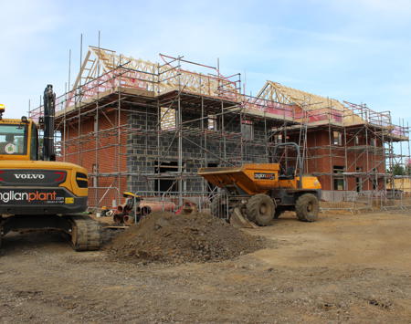 Construction Site Of Two Wooden House Frames And Two Yellow Digger On A Sunny Day