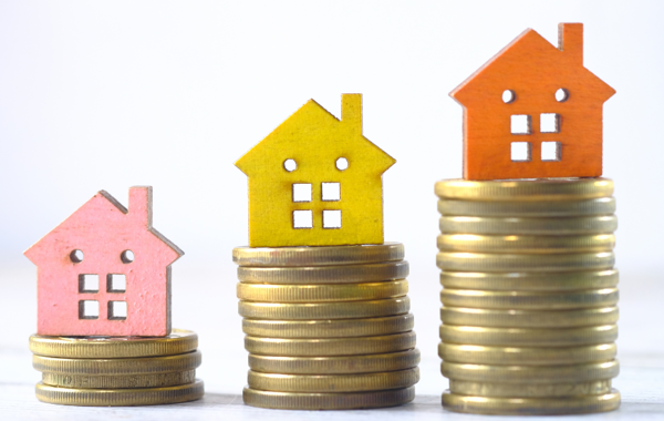Pink, Yellow And Orange House Figure On The Top Of A Pile Of Coins Increasing Height Of Pile Each Time