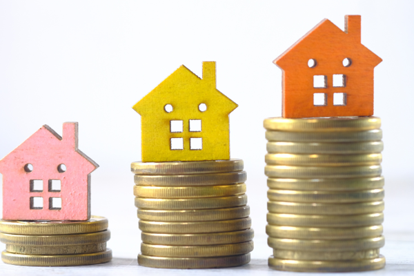 Pink, Yellow And Orange House Figure On The Top Of A Pile Of Coins Increasing Height Of Pile Each Time