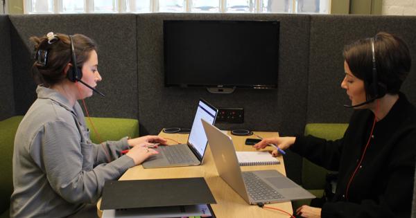 Two Members Of Saffron Sat At A Desk