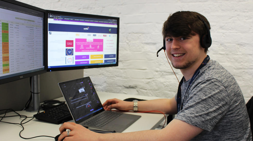 Saffron Worker Smiling At The Camera Sitting At A Computer
