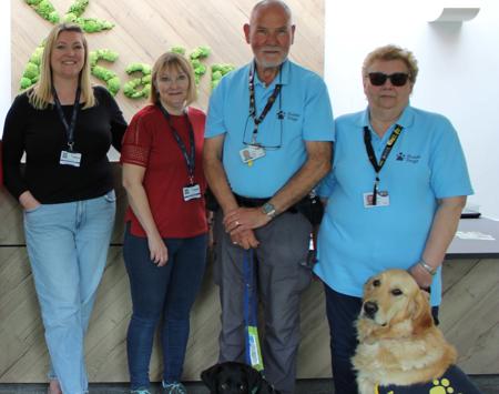 4 People Standing In A Row With A Blonde Guide Dog And A Black Guide Dog