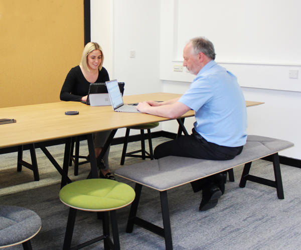 Two Members Of Staff Sat At A Project Table At Saffron Barn